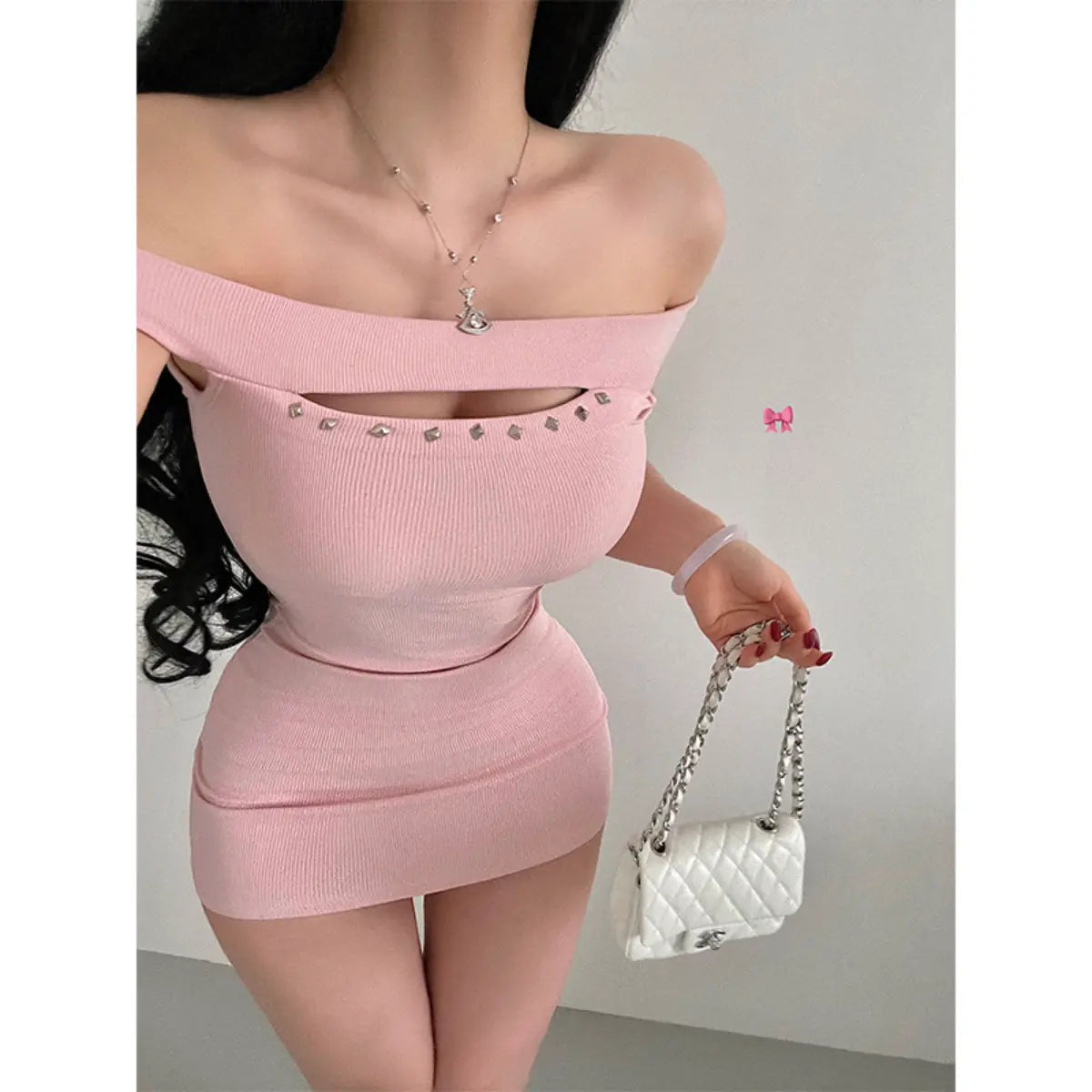 Close-up of a woman wearing a pink ribbed off-shoulder mini dress with stud details, styled with a white quilted bag.