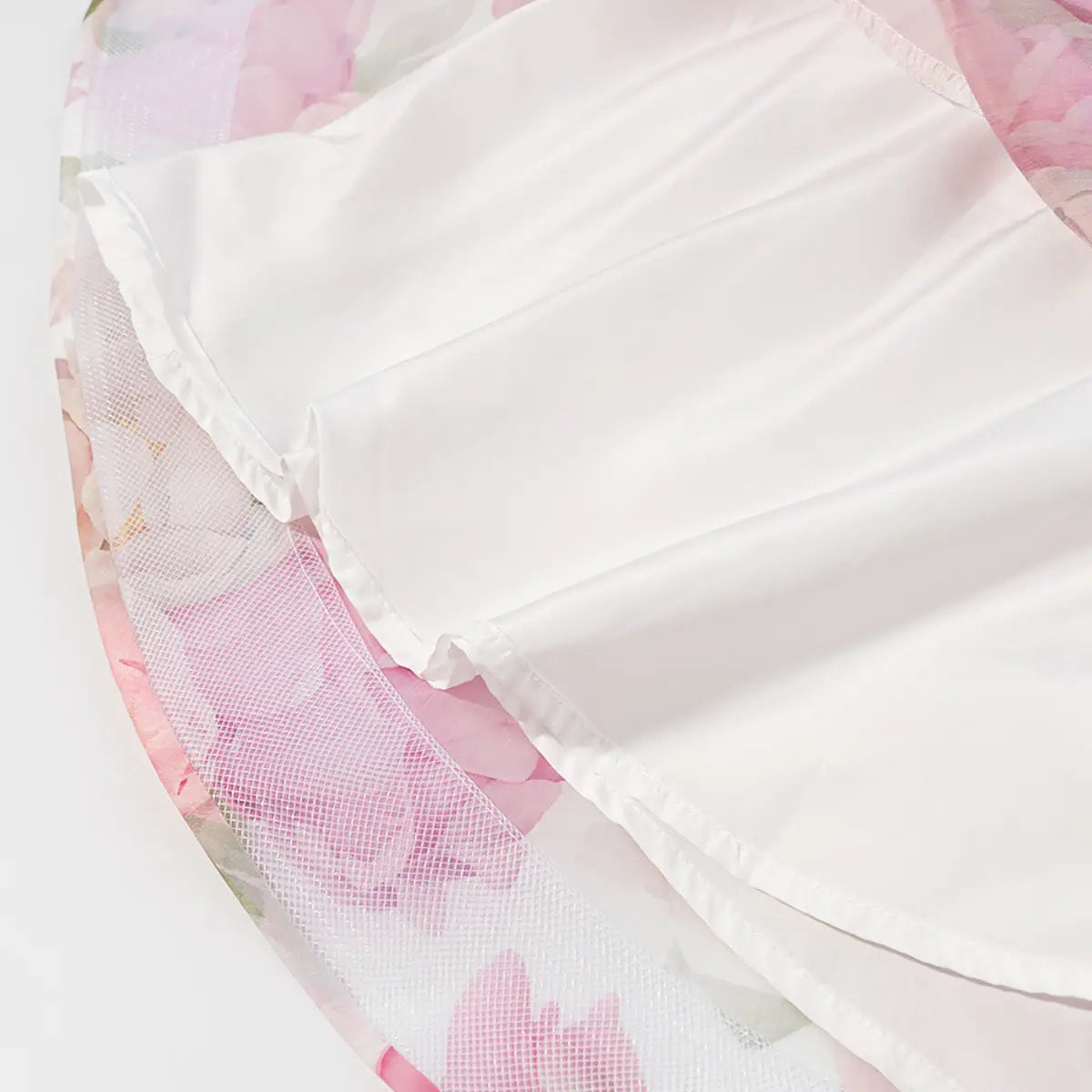  Close-up detail shot of the inner lining and ruffled hem on a pink peony floral halter dress, showing the smooth fabric and stitching.