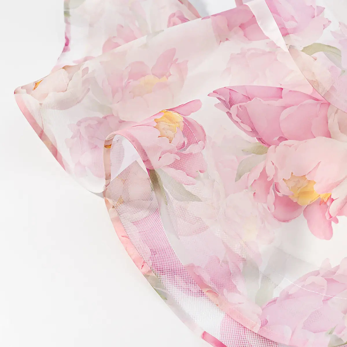 Close-up detail shot of the ruffled hem on a pink peony floral halter dress, showing the sheer overlay and mesh lining.