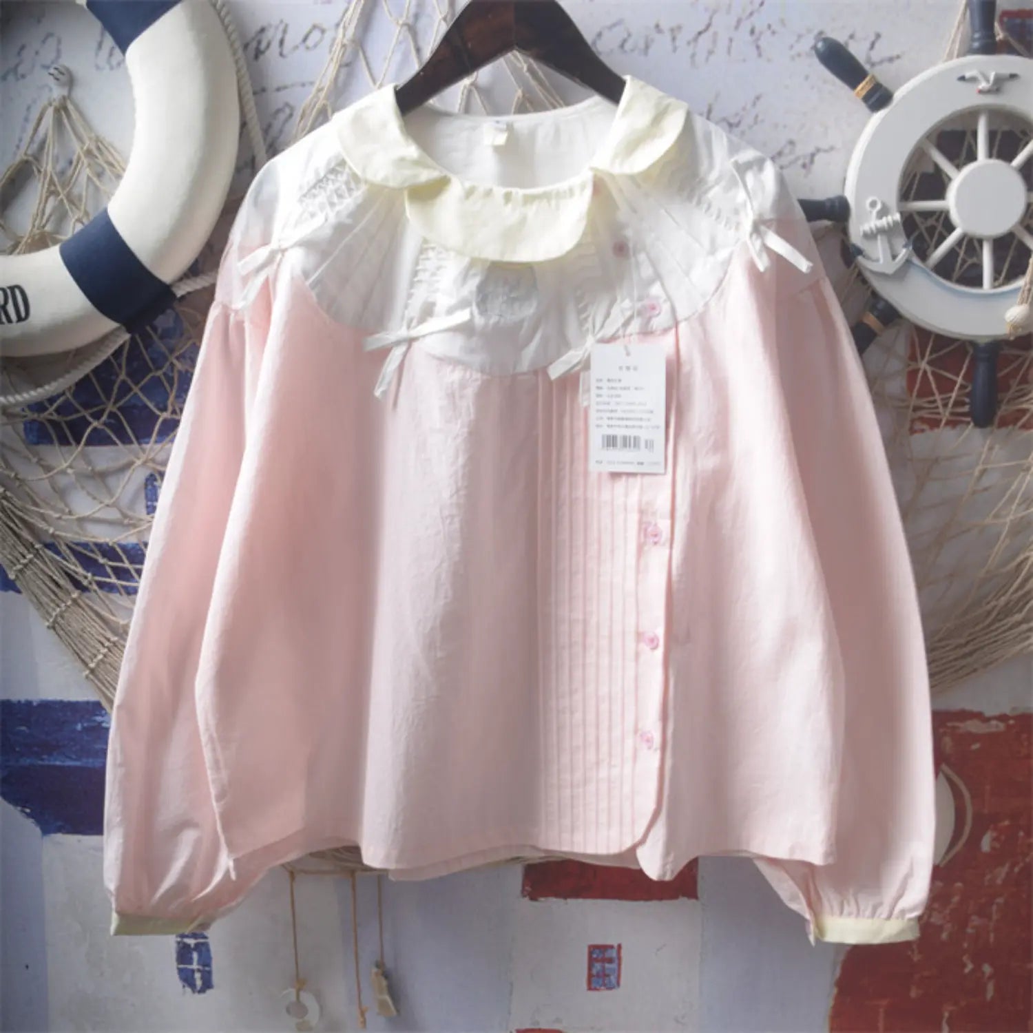 Same style light pink peter pan collar long sleeve blouse front detail shot, double layer ruffle doll collar chest embroidery badge shoulder bows front pink round buttons cuff cream trim full vertical pleated tucks craft detail display