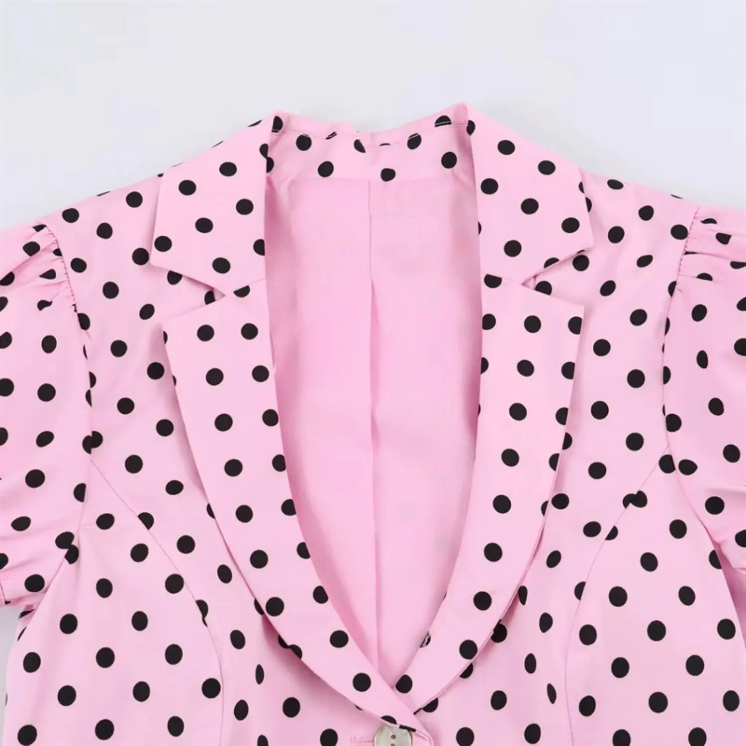 Front notch lapel close-up, open V neckline, solid pink smooth inner lining, woven polka dot outer fabric texture