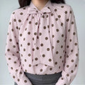 Front lifestyle shot on model, bow tie neck polka dot blouse, balloon long sleeves, matched with grey bottoms, vintage casual outfit