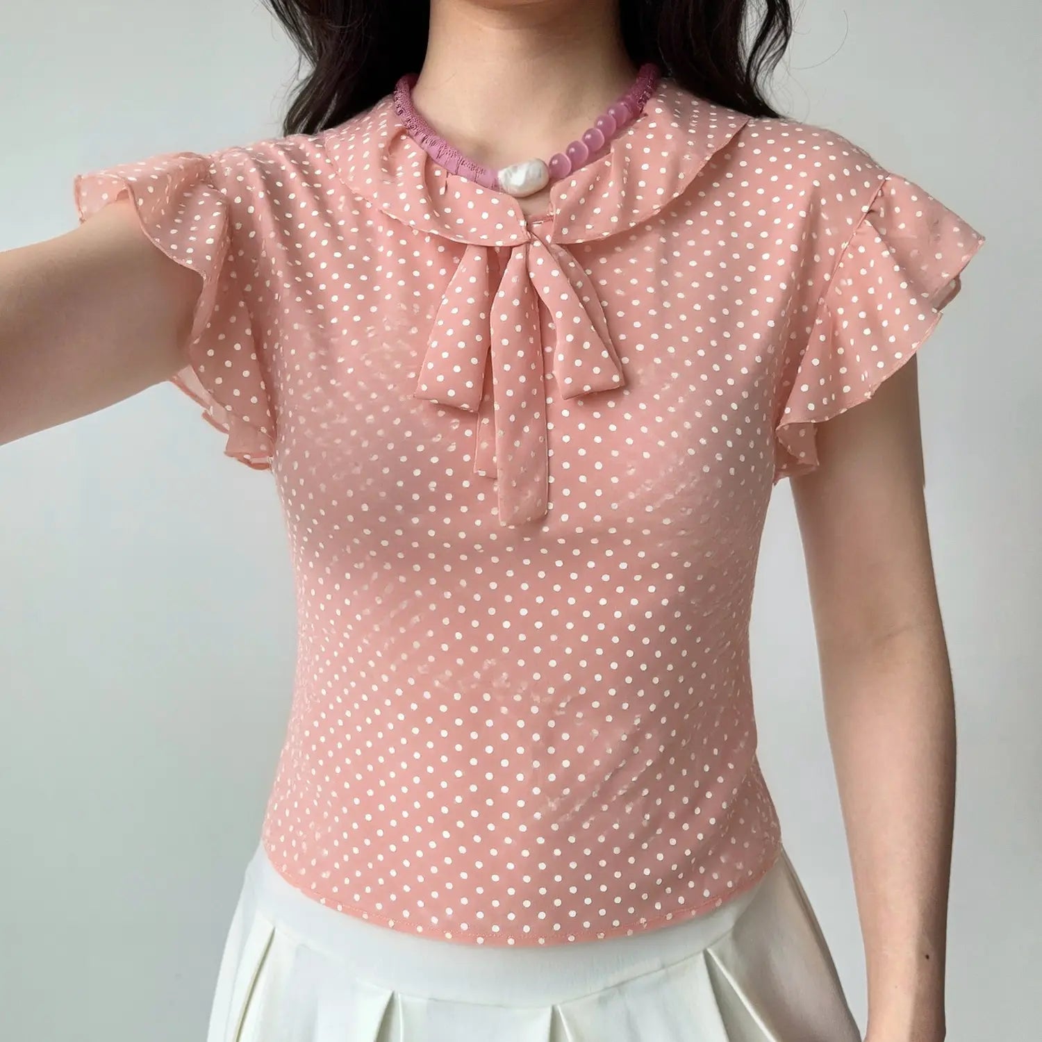 Model front view wearing pink polka dot chiffon blouse, ruffled collar tie and flutter sleeve styling