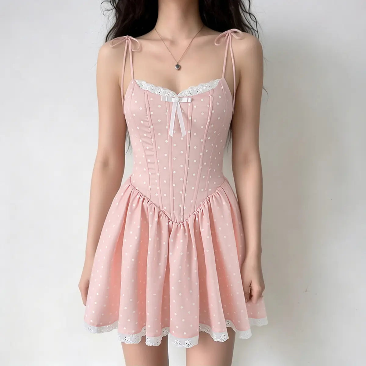 Full-body shot of a woman wearing a pink polka dot corset-style mini dress with lace trim, a white bow, and tie straps.