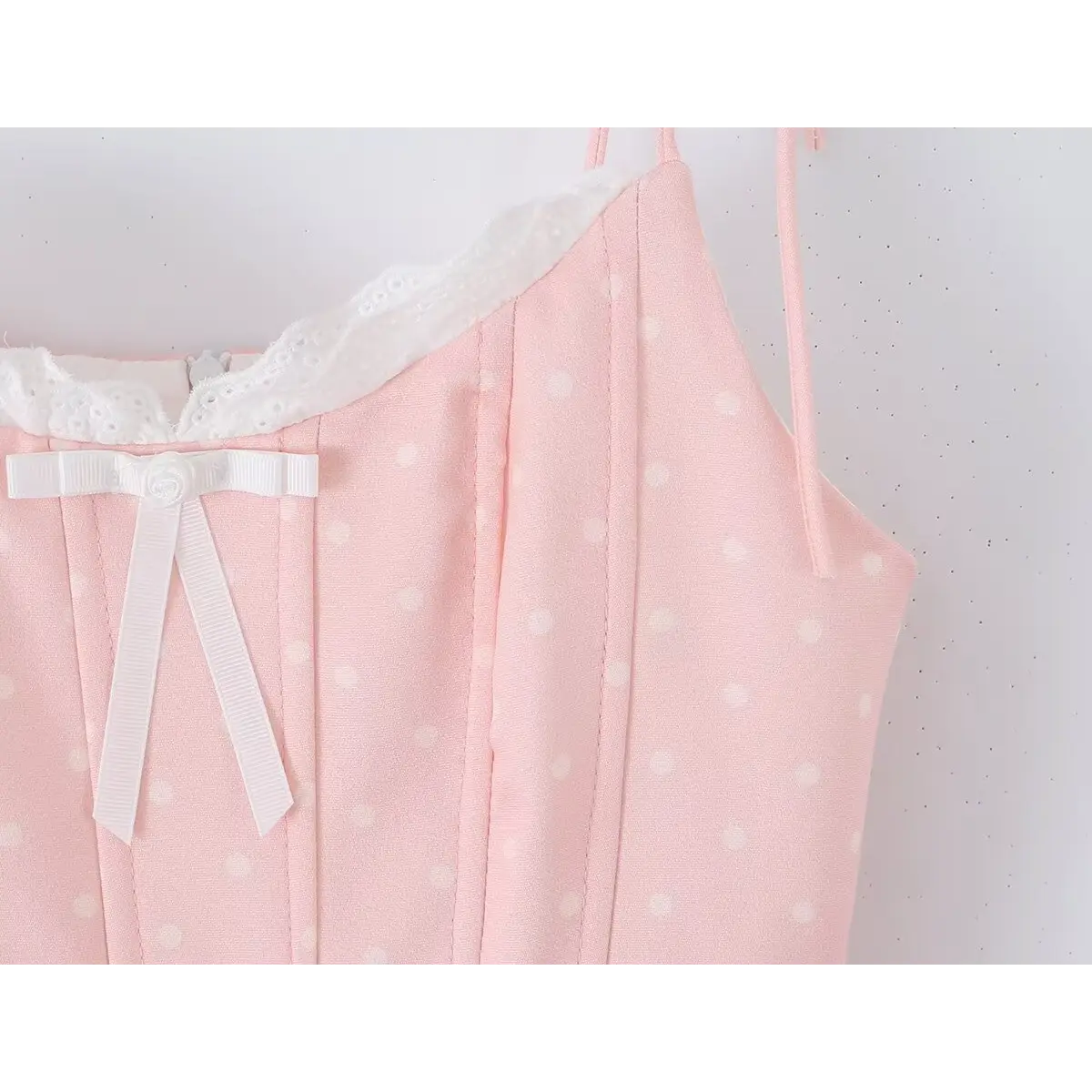 Close-up of the white bow and lace trim on the neckline of a pink polka dot dress.
