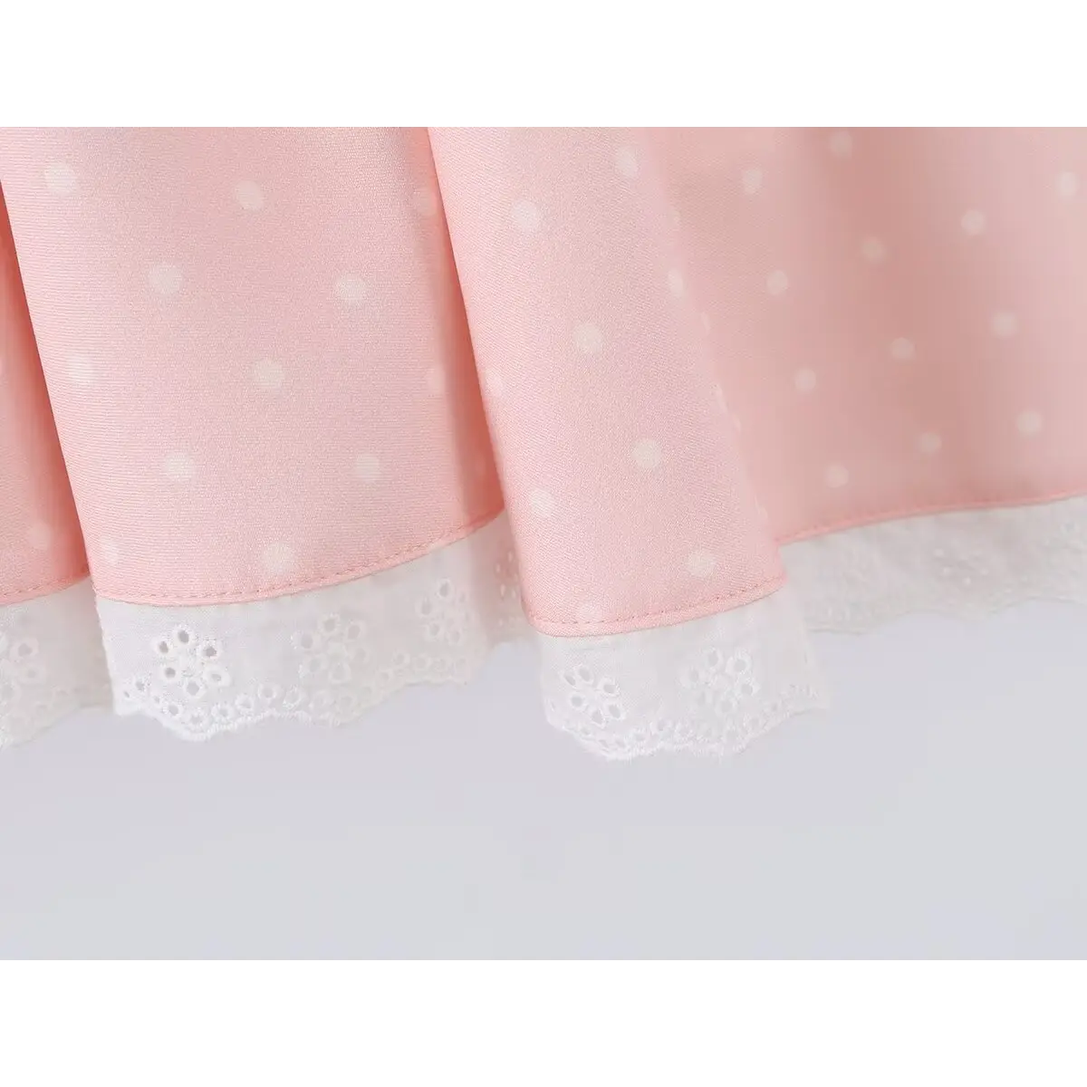 Close-up of the lace-trimmed hem on a pink polka dot dress.