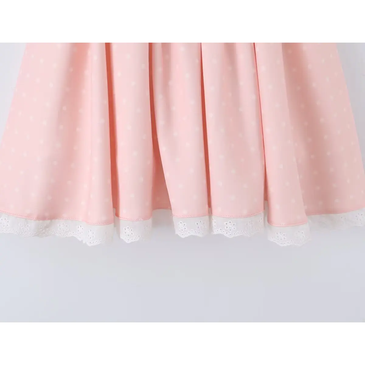 Close-up of the lace-trimmed hem on the flared skirt of a pink polka dot dress.