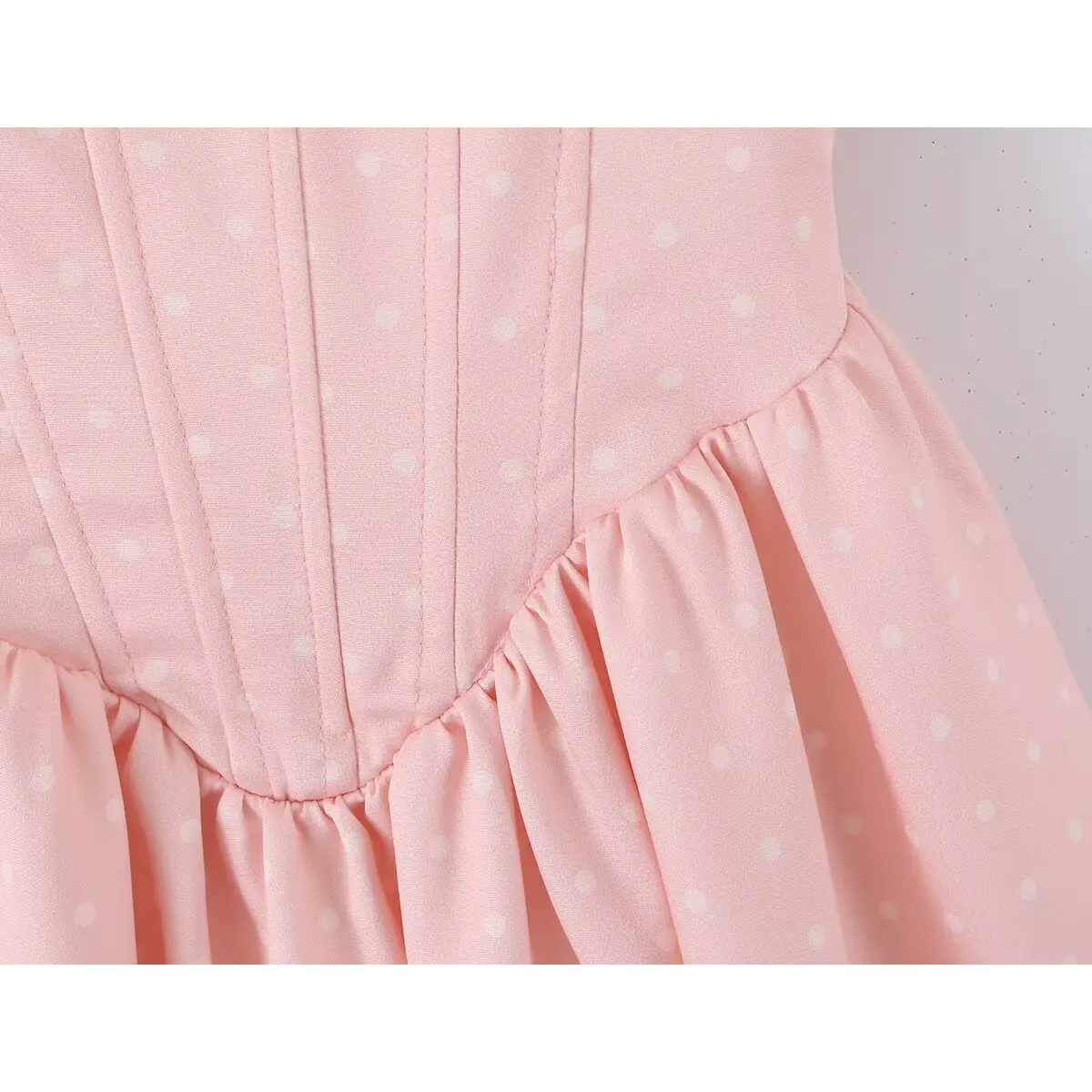 Close-up of the waist seam where the corset bodice meets the flared skirt on a pink polka dot dress.