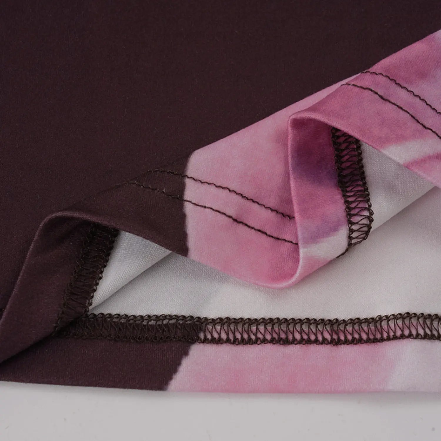 Macro close texture shot of drapeable stretch knit fabric with blended pink purple magnolia print, showcasing double parallel topstitch and elastic zigzag hem finishing on skirt edge
