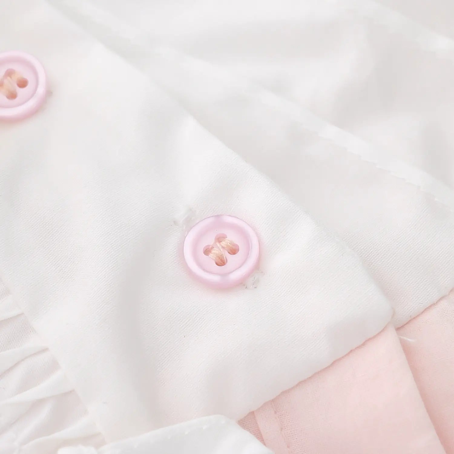 Light pink resin button placket macro close-up, matte pink round buttons double secure stitching neat binding white spliced yoke front placket craft detail shot
