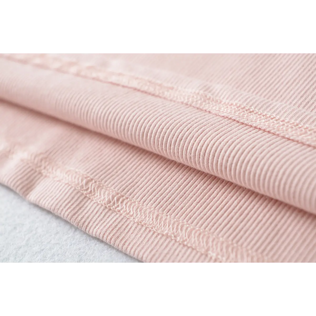 Close-up of the hem and stitching on a pink ribbed dress, showing the fabric texture.