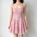 Model wearing a pink rose-embroidered organza sundress with spaghetti straps, square neckline, fitted corset-style bodice, and flared skirt, holding a brown handbag.