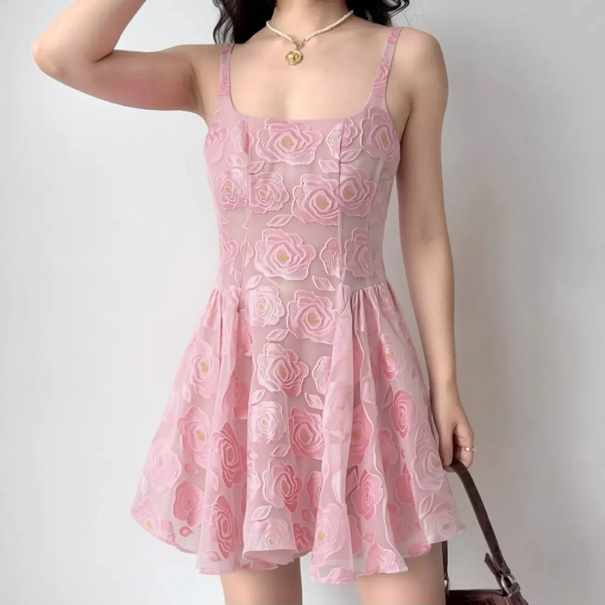 Model wearing a pink rose-embroidered organza sundress with spaghetti straps, square neckline, fitted corset-style bodice, and flared skirt, front view.
