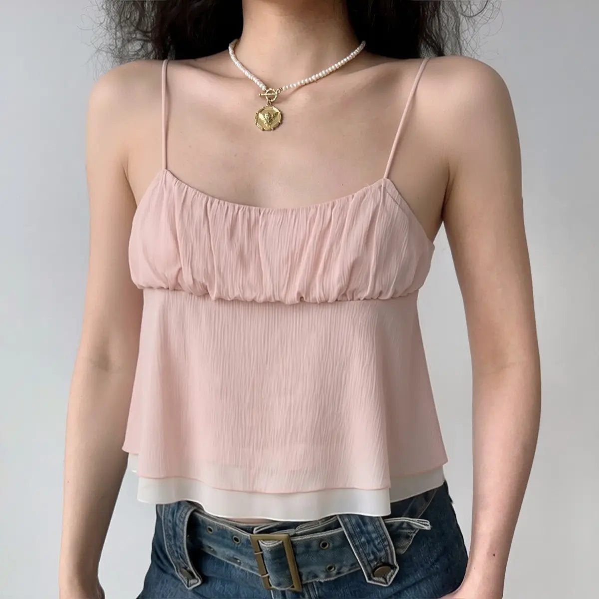  Model wearing a light pink ruffled cami top with jeans, showcasing the flowy silhouette, gathered bust, and sheer double-layered hem.