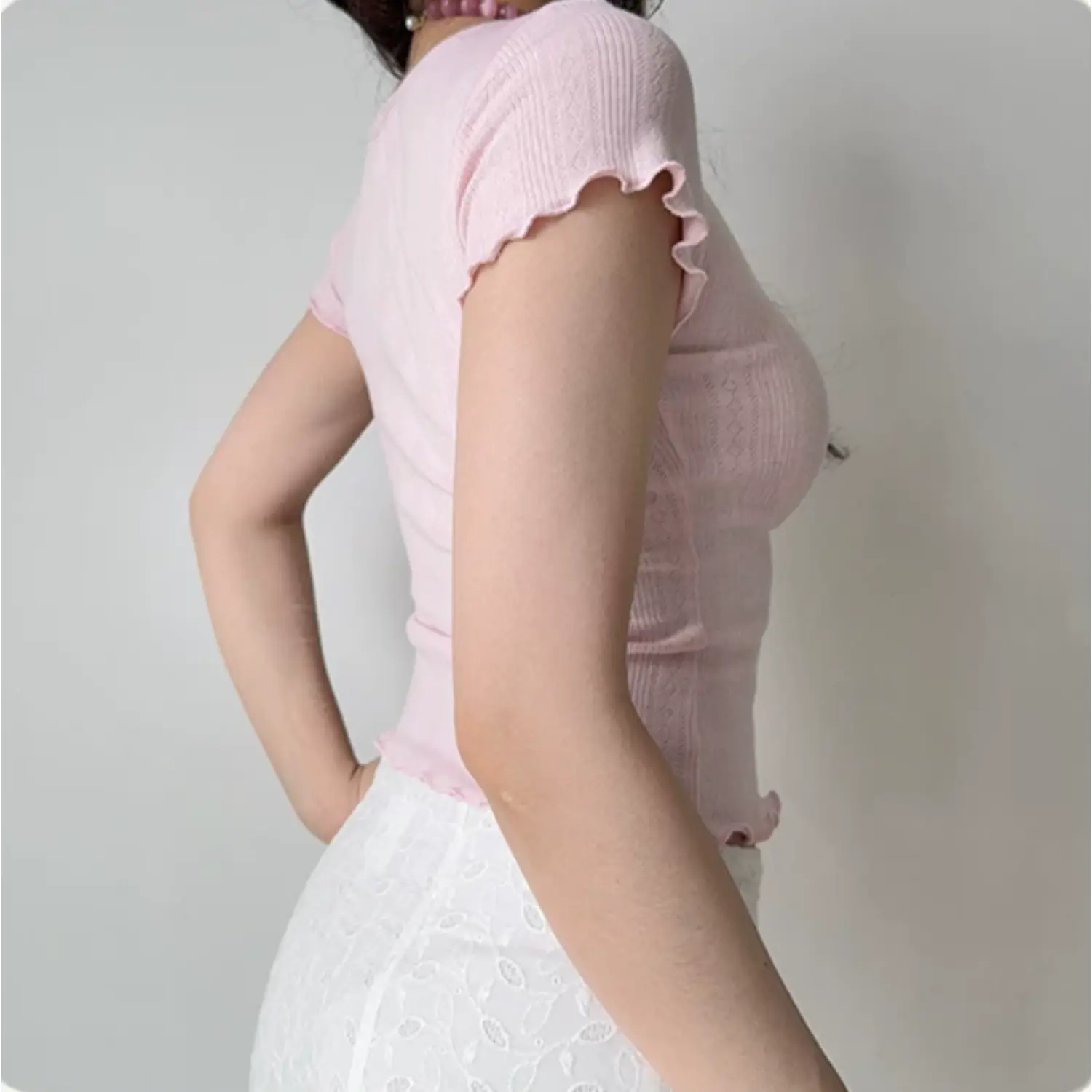 Side/back view of model wearing the pink ribbed knit top, showing the fitted silhouette and scalloped sleeve hem
