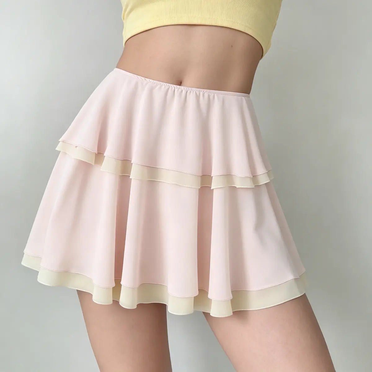 Front view of a light pink tiered chiffon mini skirt, highlighting the double-layer construction, contrast beige trim, and elasticated waistband.