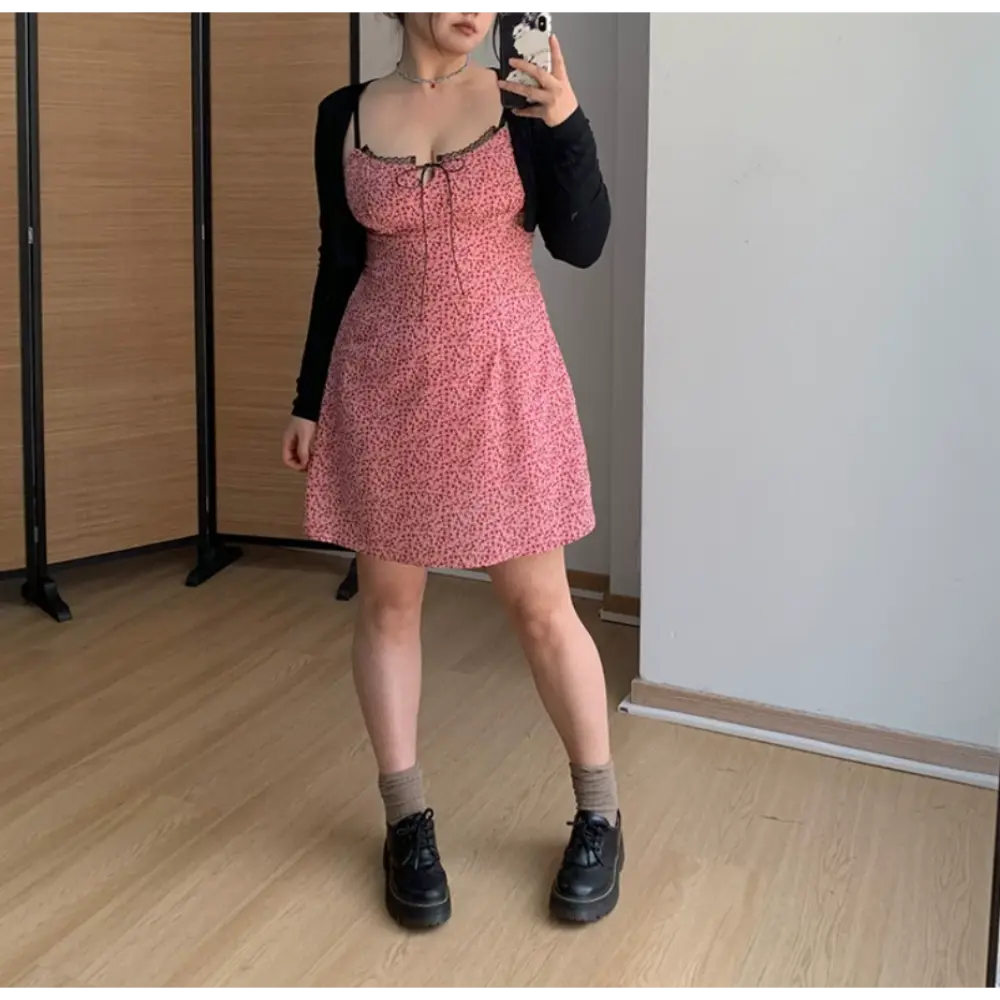 Straight front indoor mirror lifestyle photo of pink ditsy floral spaghetti strap mini dress, lightweight black layering cardigan, casual gray crew socks and platform doc style shoes