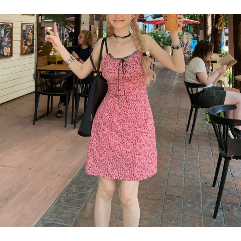 Full body outdoor street cafe lifestyle shot of pink micro floral slip mini dress, double braid hairstyle, model holding orange drink cup and making peace hand gesture