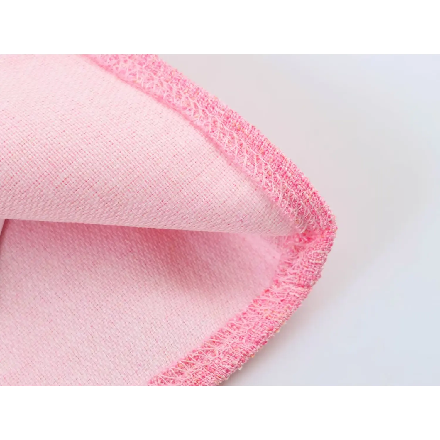 Macro shot of fabric cross-section, showing outer textured pink tweed and smooth solid pink lining with neat overlock hem stitching