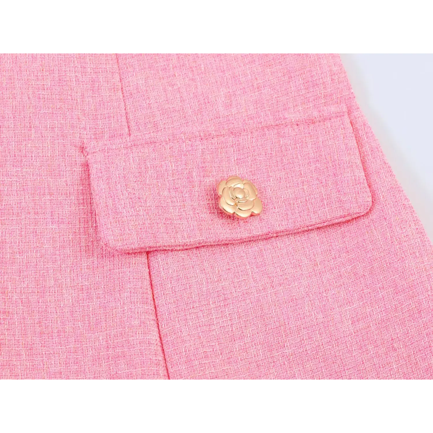 Close-up of front patch pocket decorated with gold 3D camellia metal button, textured pink mixed tweed fabric