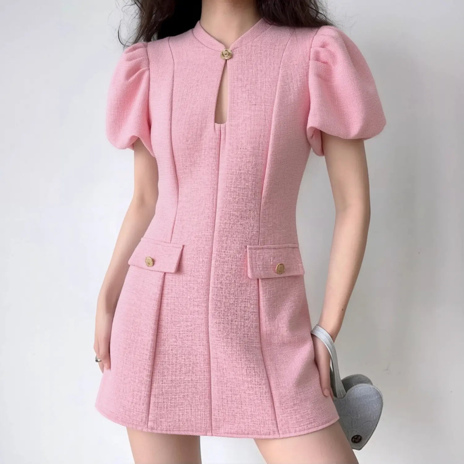 Lifestyle full-body outfit photo of model wearing pink tweed cheongsam mini dress with puff sleeves, paired with gray heart-shaped shoulder bag
