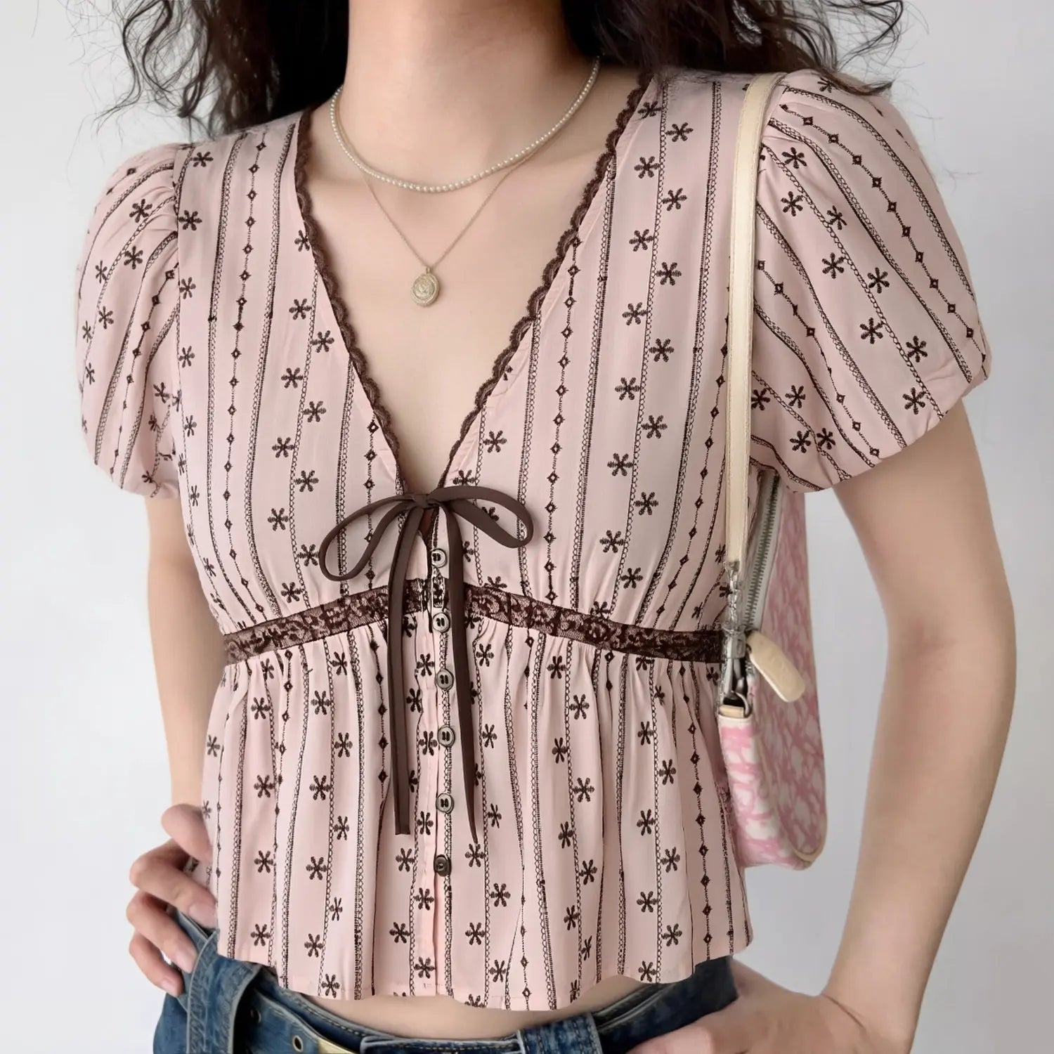 Front lifestyle shot on model of pink floral stripe blouse, V neck lace & ribbon detail, puff sleeves, fitted peplum waist, sweet vintage casual top