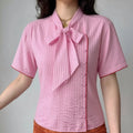 Front lifestyle shot on model of tie neck striped blouse, fitted waist, red edge piping detail