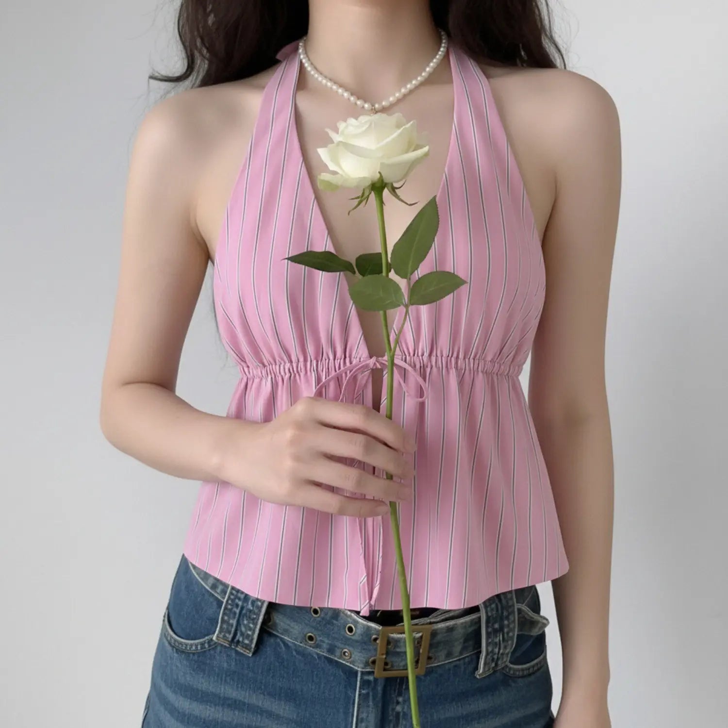 Front lifestyle shot on model of pink vertical stripe halter cami top, V neck, front drawstring tie waist, sleeveless cropped vacation blouse