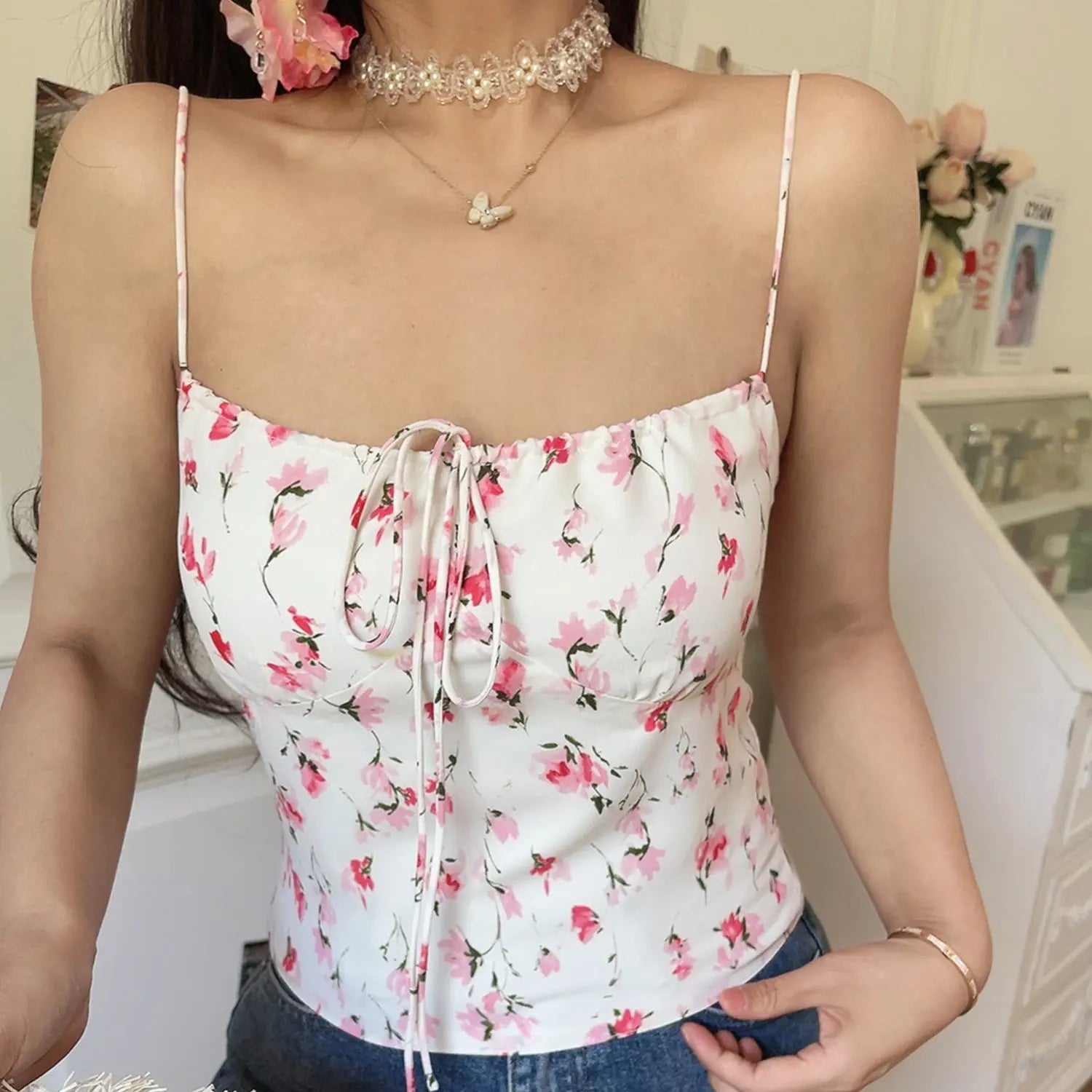White base pink rose watercolor floral cami crop top, adjustable front tie thin printed straps, full front model shot against white decor wall