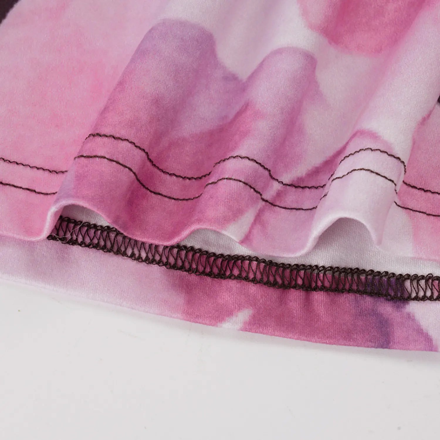 Macro close texture shot of stretch knit fabric with blended pink purple magnolia print, showcasing double parallel topstitch and elastic zigzag hem finishing