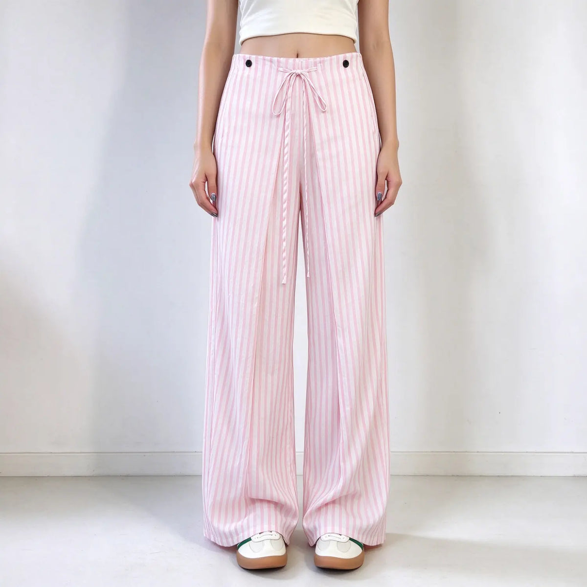 Model wearing pink and white stripe wide leg pants, high waist with drawstring and button details, lightweight fabric, loose fit, paired with white cropped top, plain white background