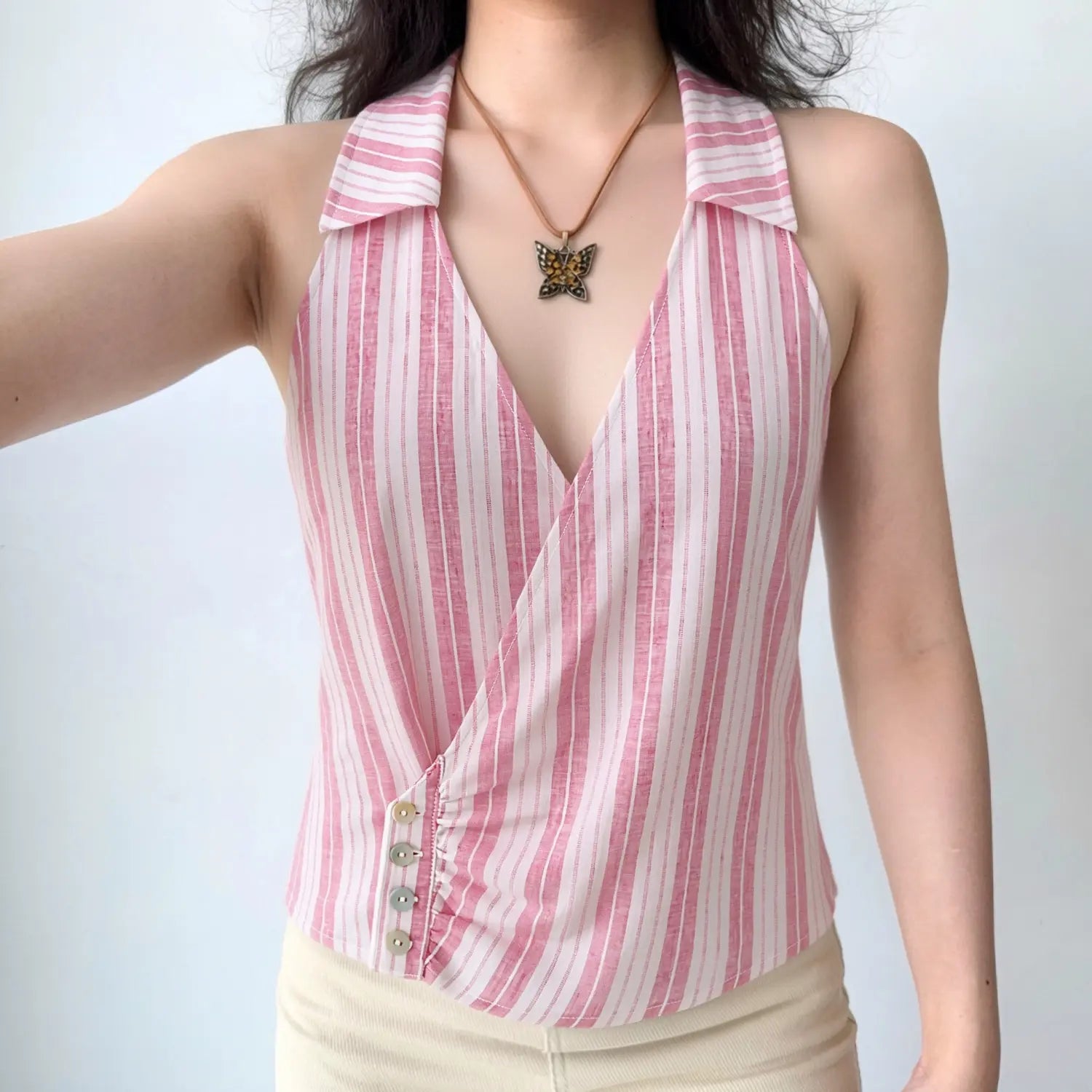 Front lifestyle shot on model of pink white vertical stripe halter wrap crop top, lapel collar, side shell button detail, summer casual outfit
