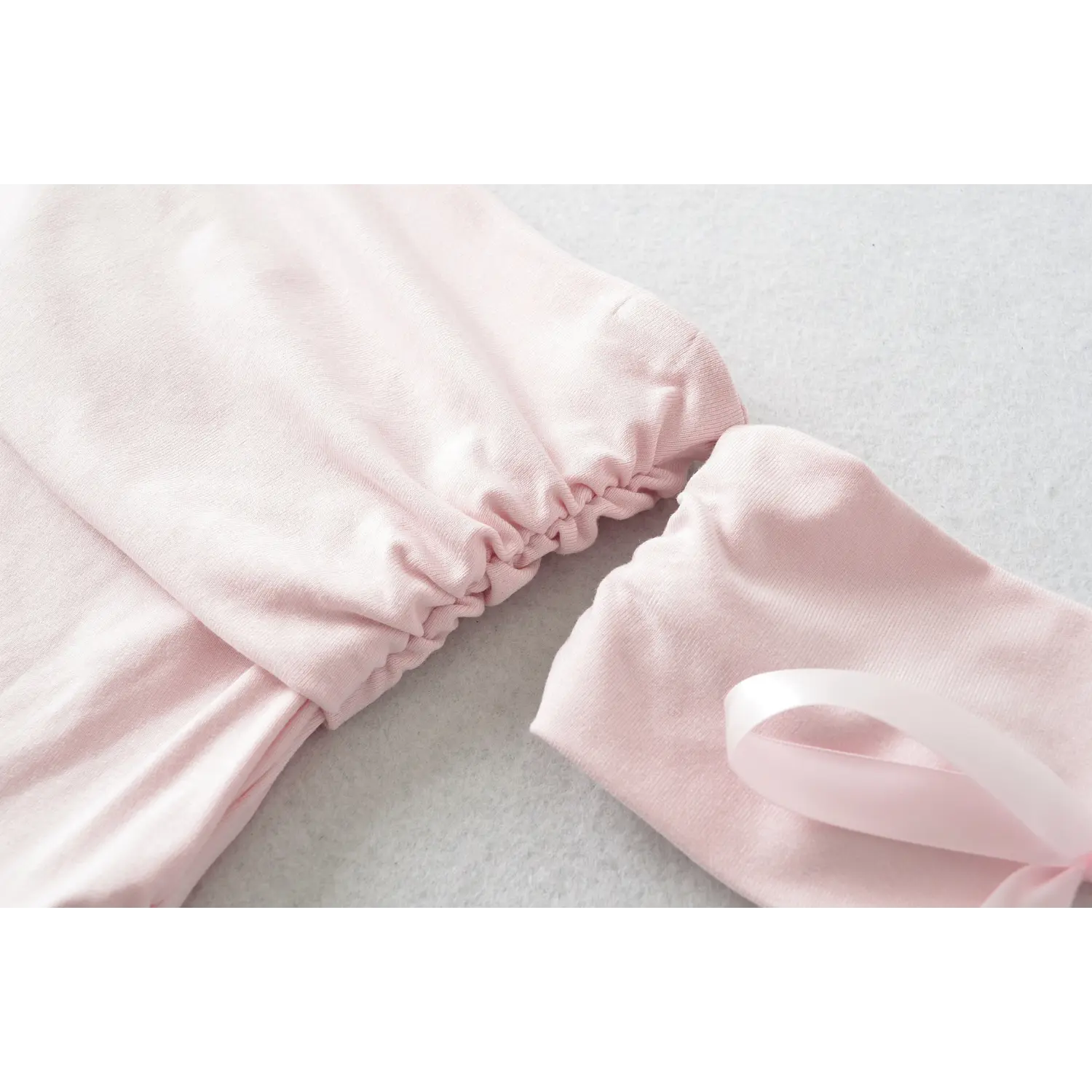 Fabric detail of side ruching and connecting seam between pink off shoulder top and bow sleeve