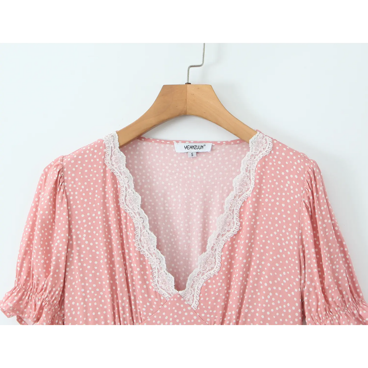 Close‑up of lace v‑neck collar, pink polka dot dress hanging on wood hanger