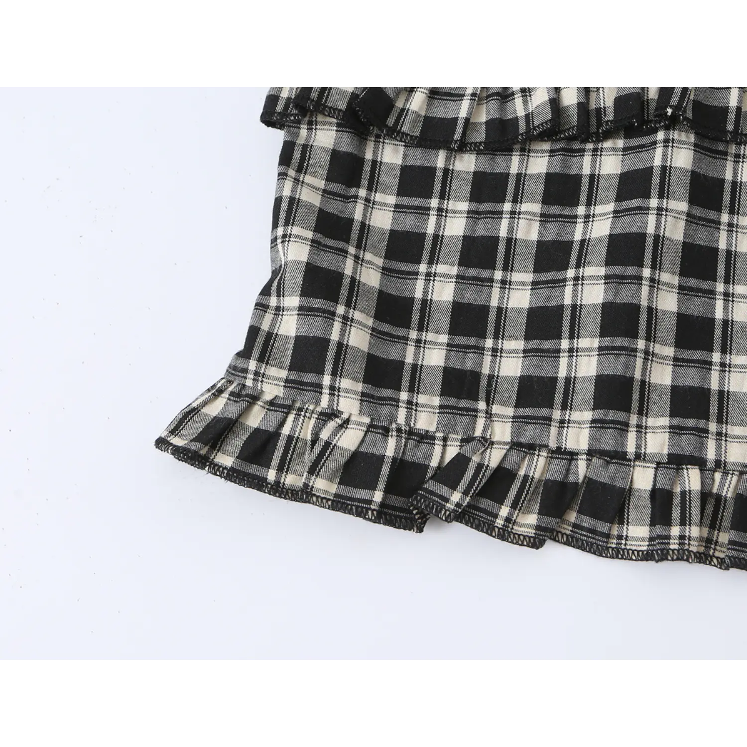Close-up of black cream plaid blouse ruffle hem, neat serged zigzag stitching, lightweight woven check fabric frill detail