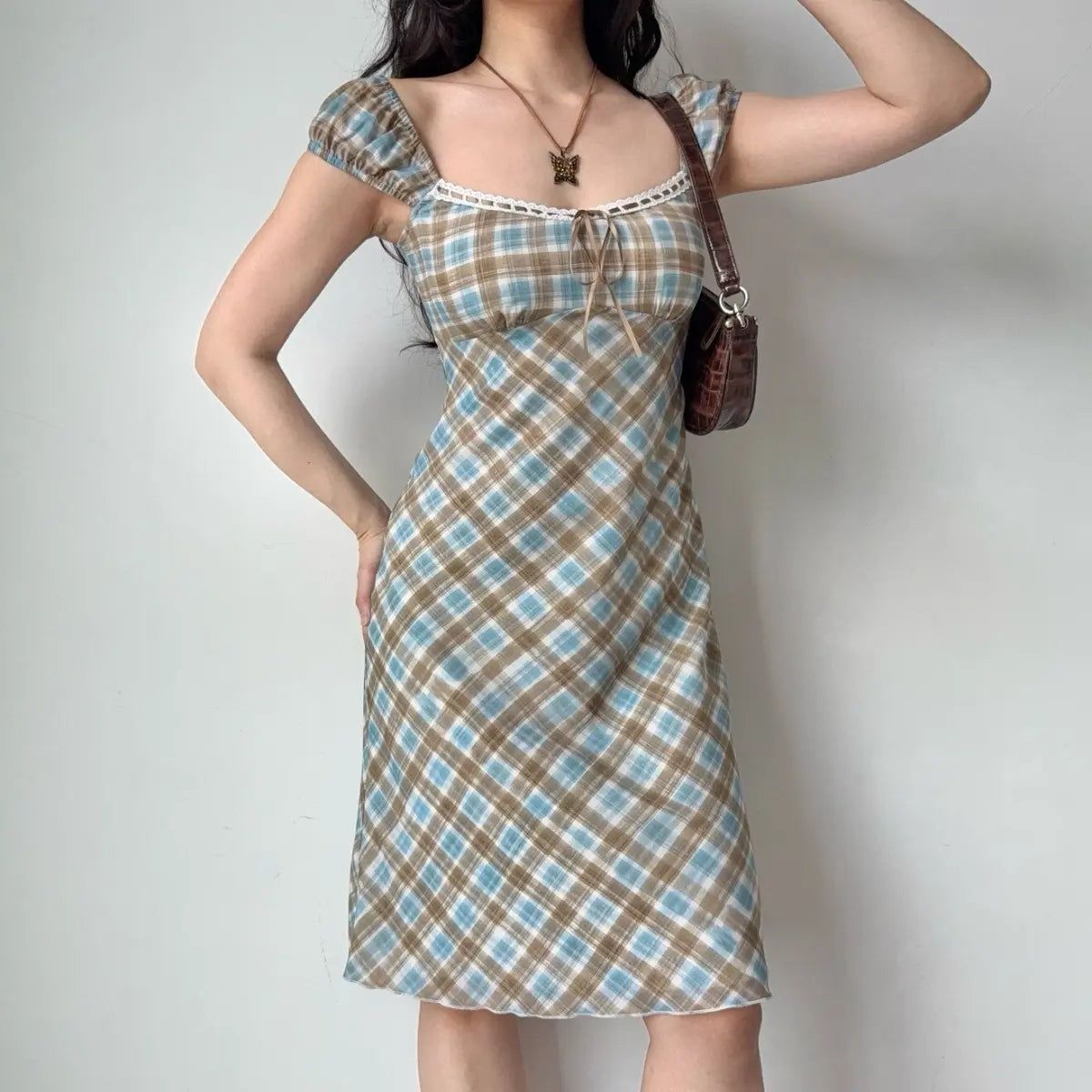 The blue and brown plaid dress paired with a butterfly necklace, highlighting the lace-trimmed neckline.
