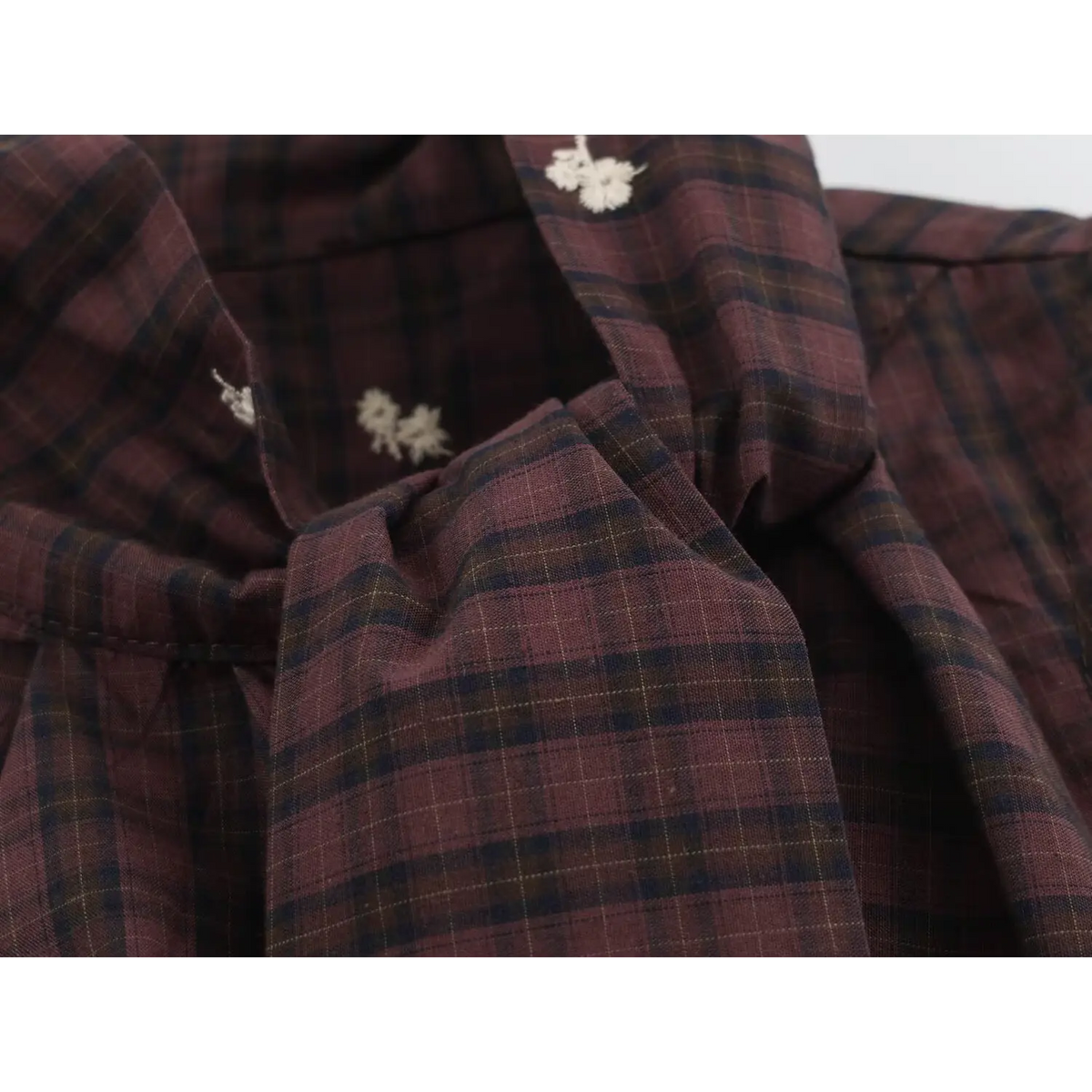 Close-up of collar area with white embroidered flowers on wine red and navy plaid fabric