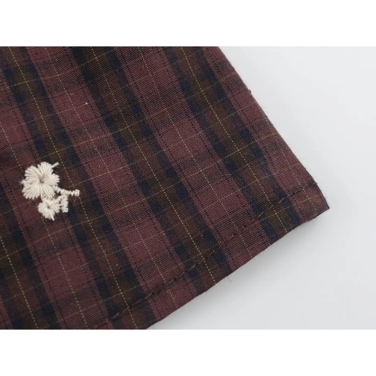 Close-up of wine red and navy plaid fabric with fine yellow check lines, white floral embroidery and neat edge stitching