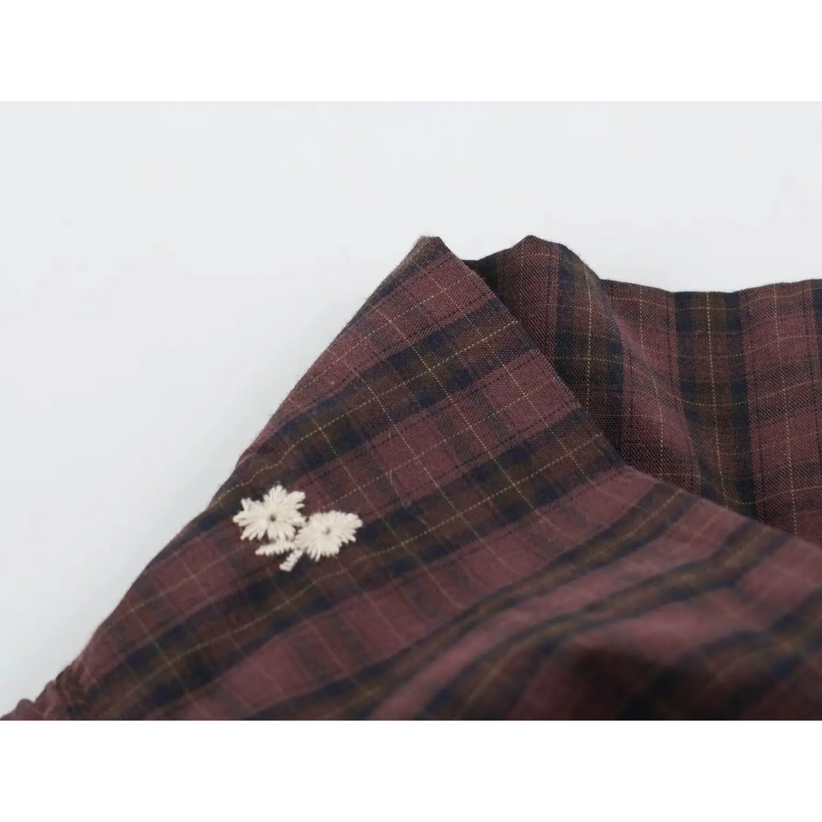 Close-up of folded wine red and black plaid fabric with two white embroidered flowers