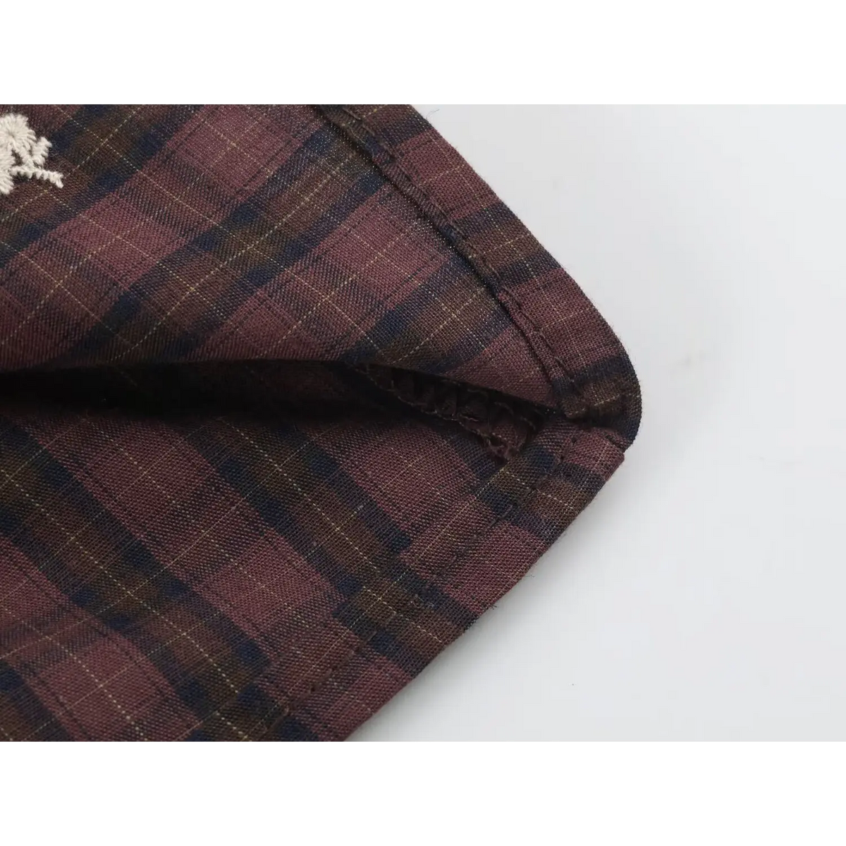 Close-up of plaid fabric with white floral embroidery and seam with fabric edge details