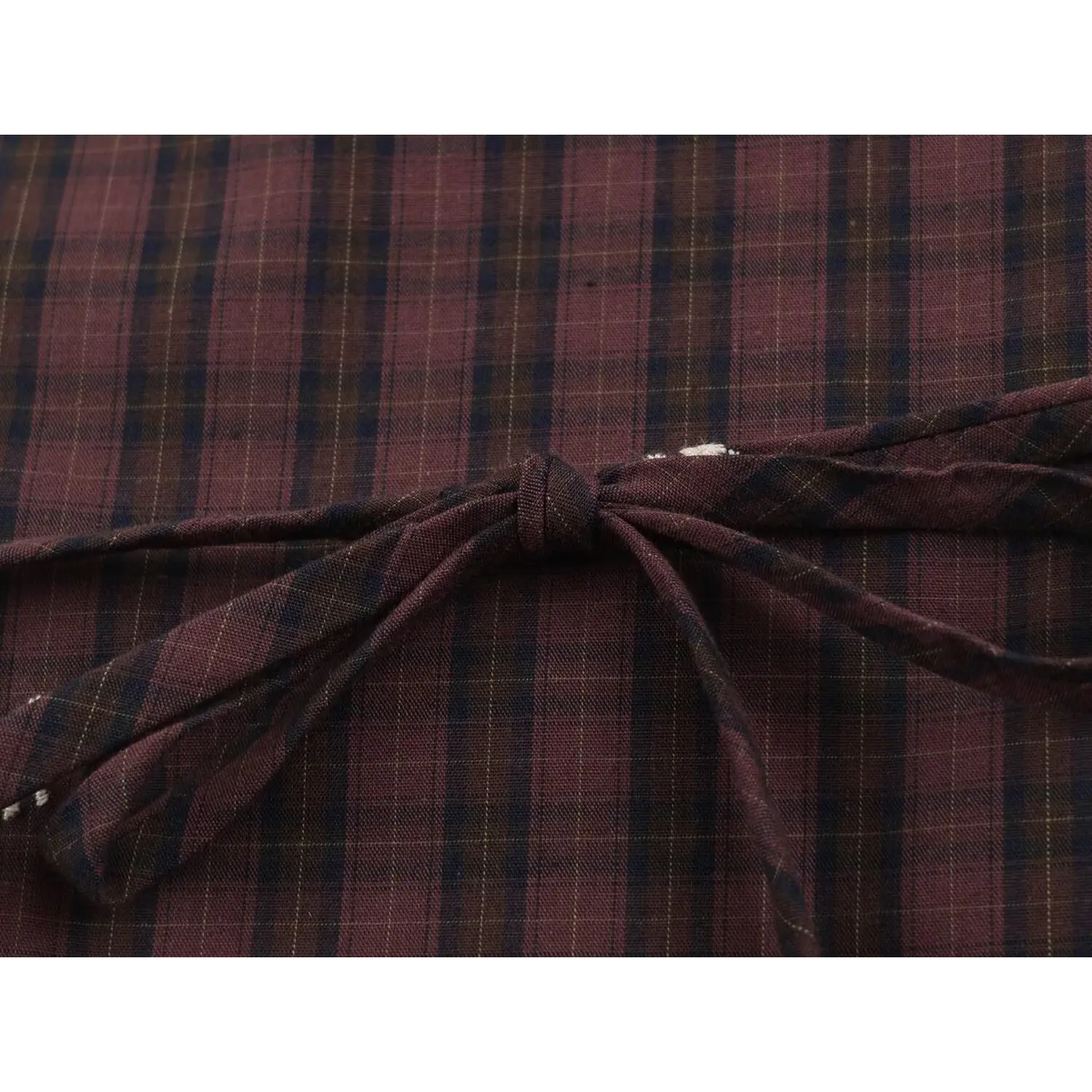 Close-up of matching fabric tie knot on plaid vest with loose white threads