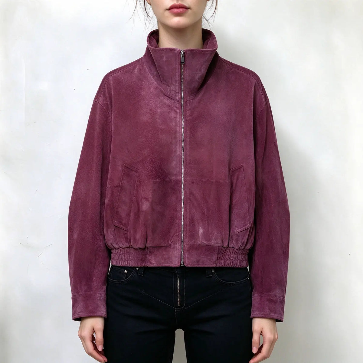 Model wearing plum suede bomber jacket, high stand collar, full front metal zipper, side patch pockets, elastic ribbed hem, long sleeves, relaxed cropped fit, paired with black jeans, plain white background