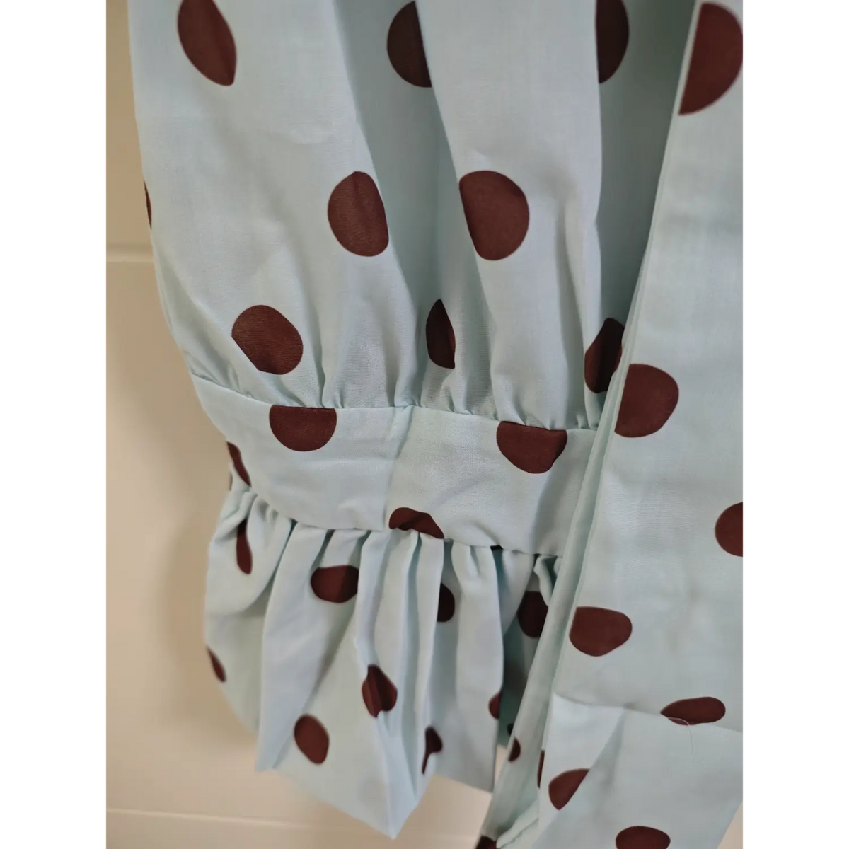 Close-up detail of polka dot blouse elasticated peplum waist and ruffle hem, light blue fabric with big brown dots