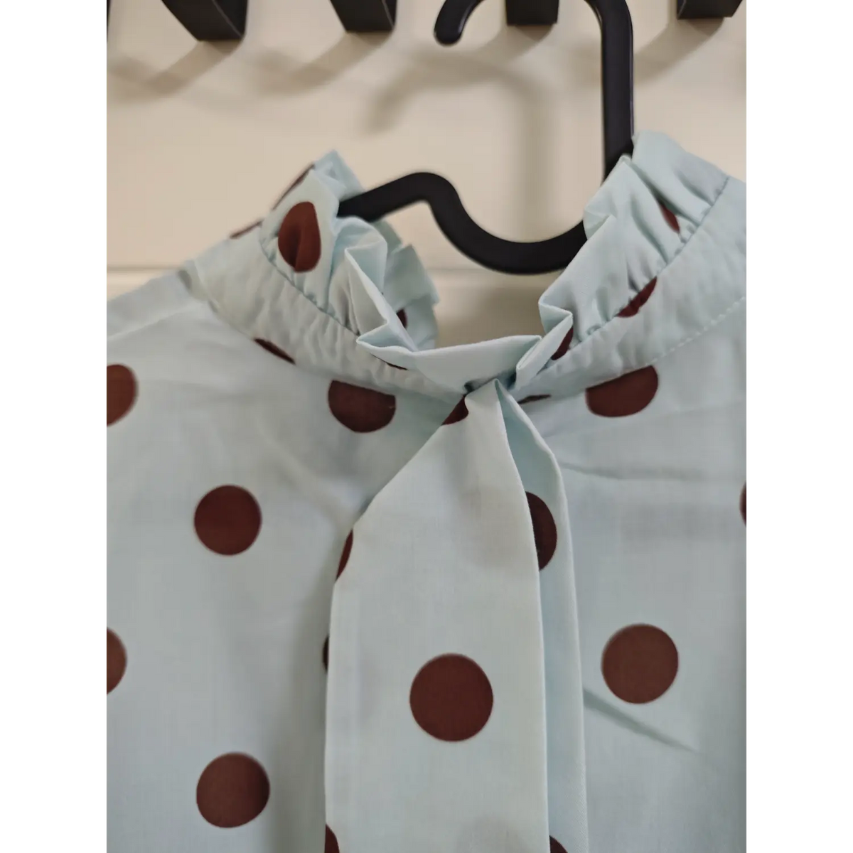 Macro shot of ruffle frilled stand collar and neck tie on light blue brown polka dot blouse