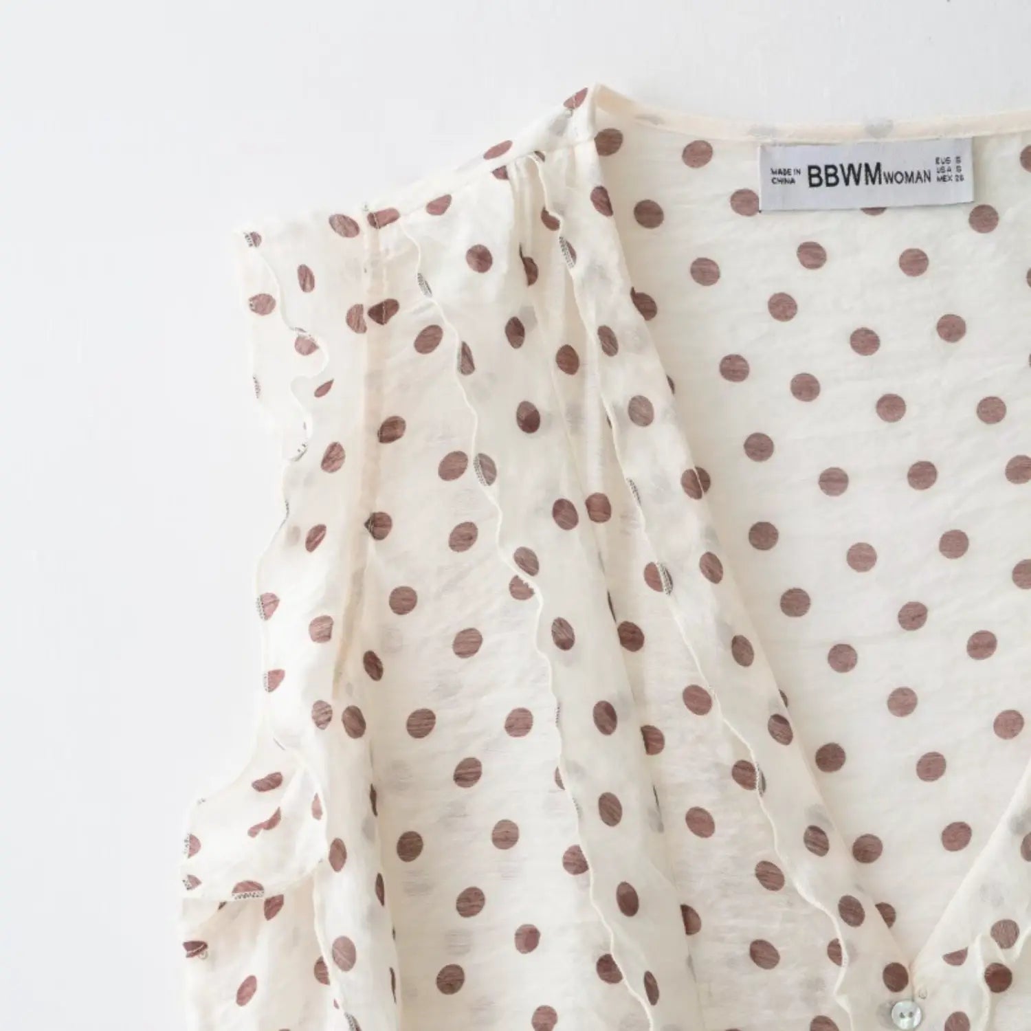 Partial close-up of deep V neckline and vertical wavy lettuce edge ruffles, brown polka dot lightweight textured fabric