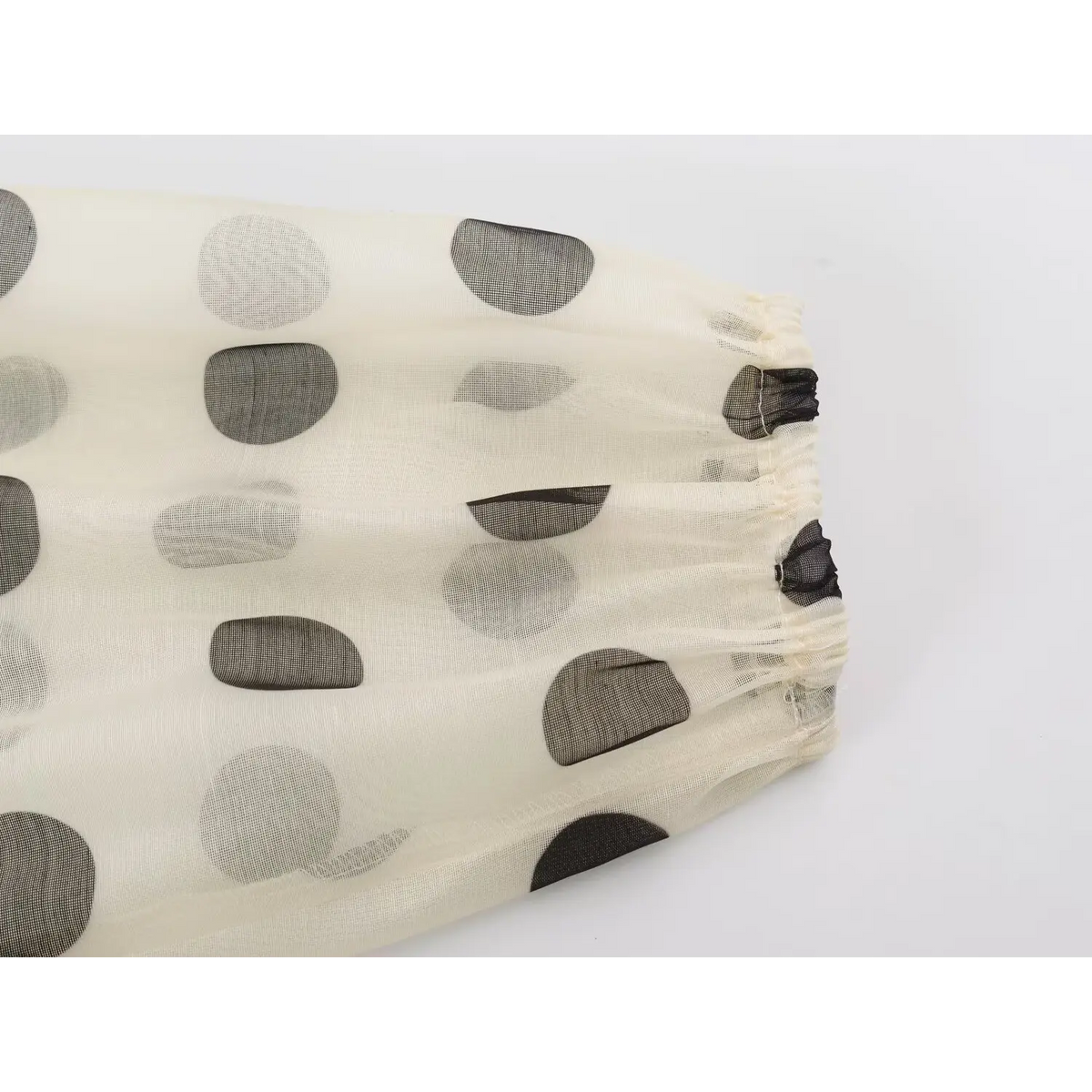 Close-up of polka dot mesh fabric with gathered edge and black elastic trim
