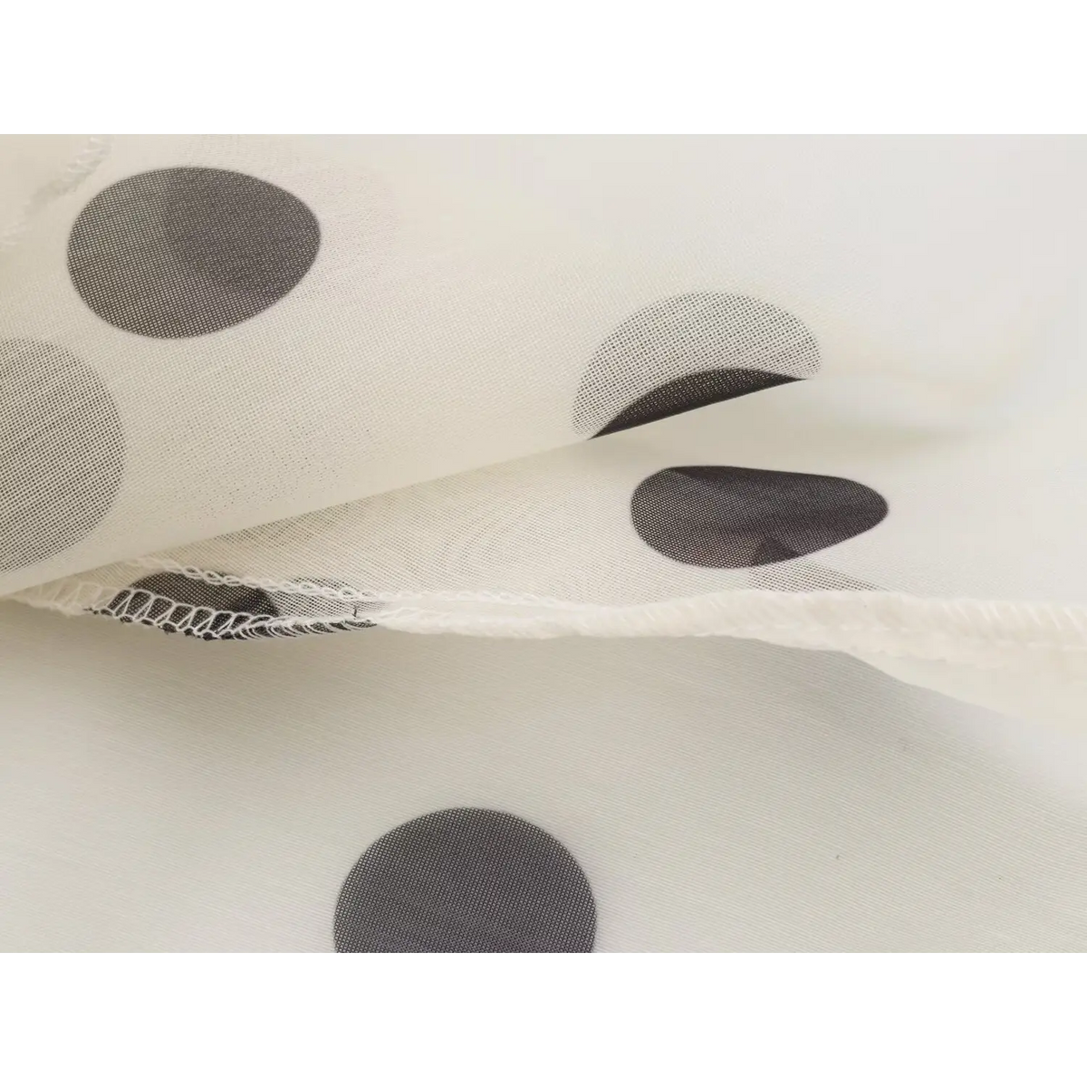 Close-up of folded cream mesh fabric with black polka dots and stitched edges