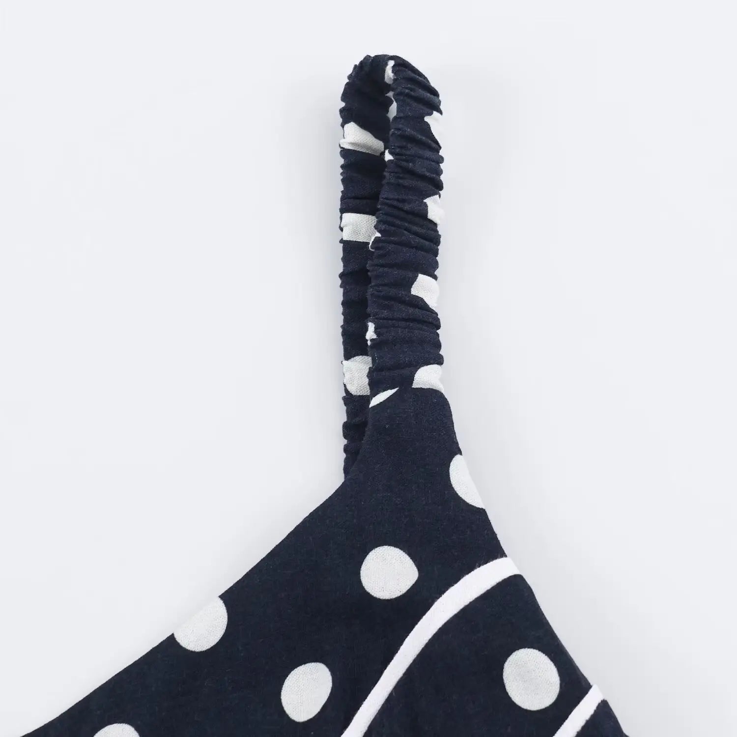 Partial close‑up of smocked elastic spaghetti strap, navy polka dot woven fabric, gathered stretch construction