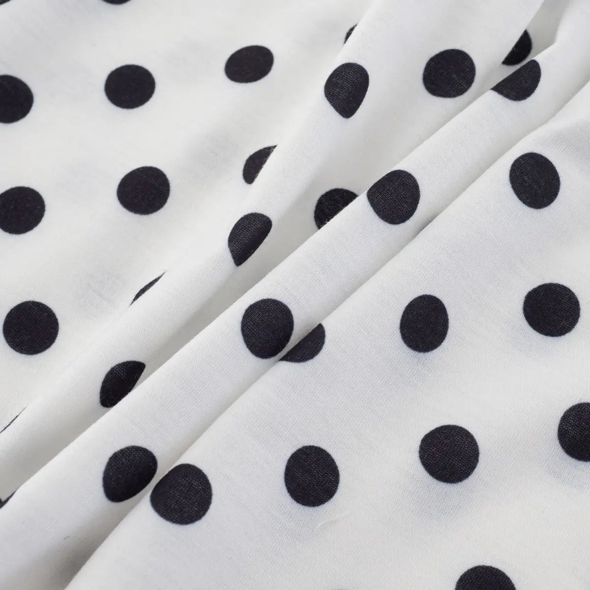Close-up texture shot of white fabric with black polka dots, showing soft knit material and slight drape.