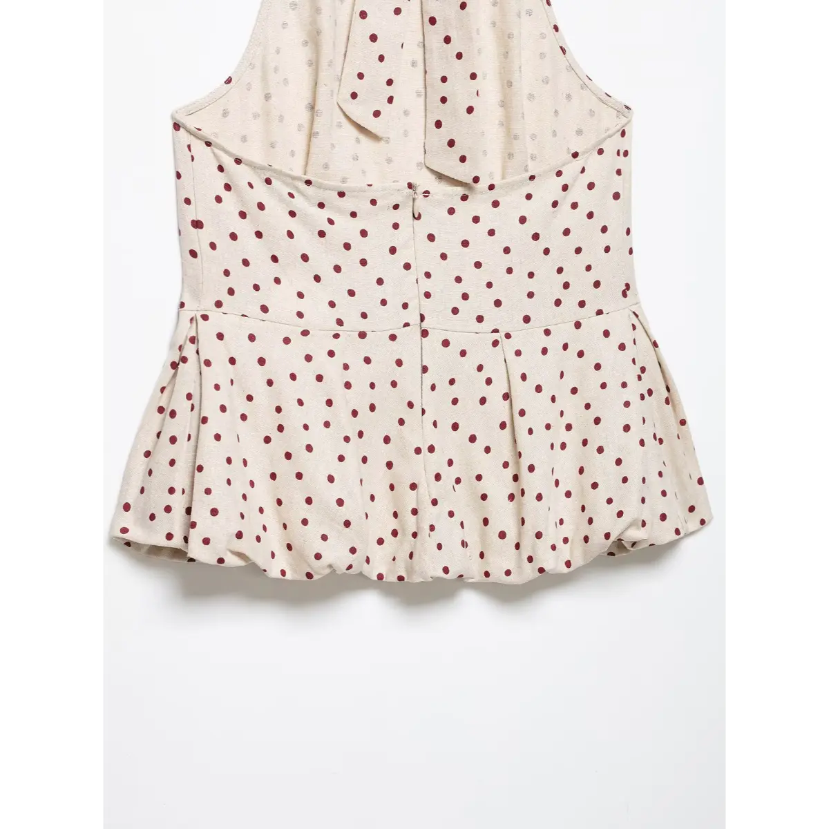 Back view of a beige halter top with red polka dots, showing the central zipper closure, tie detail, and peplum hem.